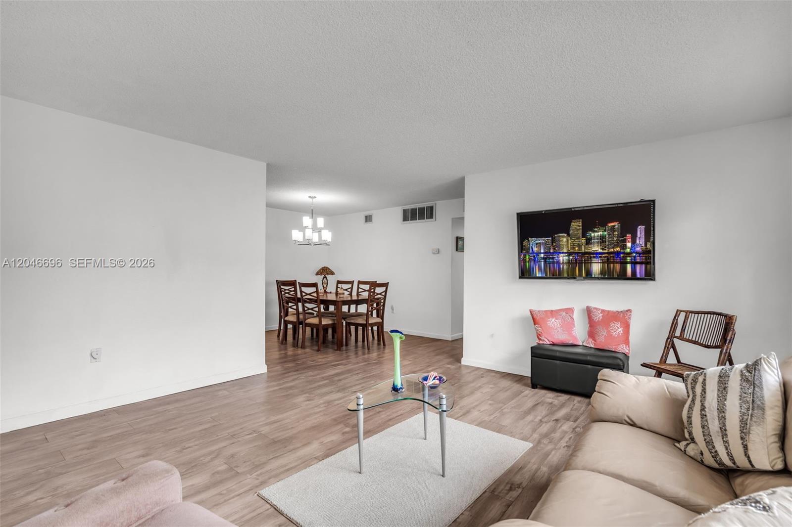 A living room with wood-look flooring flows into a dining area with a chandelier — 20327 NE 2nd Ave # 26, Miami FL 33179, MIAMI, FL