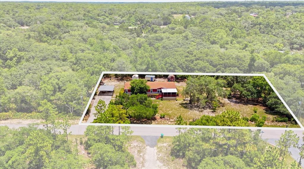 An aerial view shows a red house with a carport on a wooded lot — 1391 S GETTYSBURG DRIVE, HOMOSASSA, FL