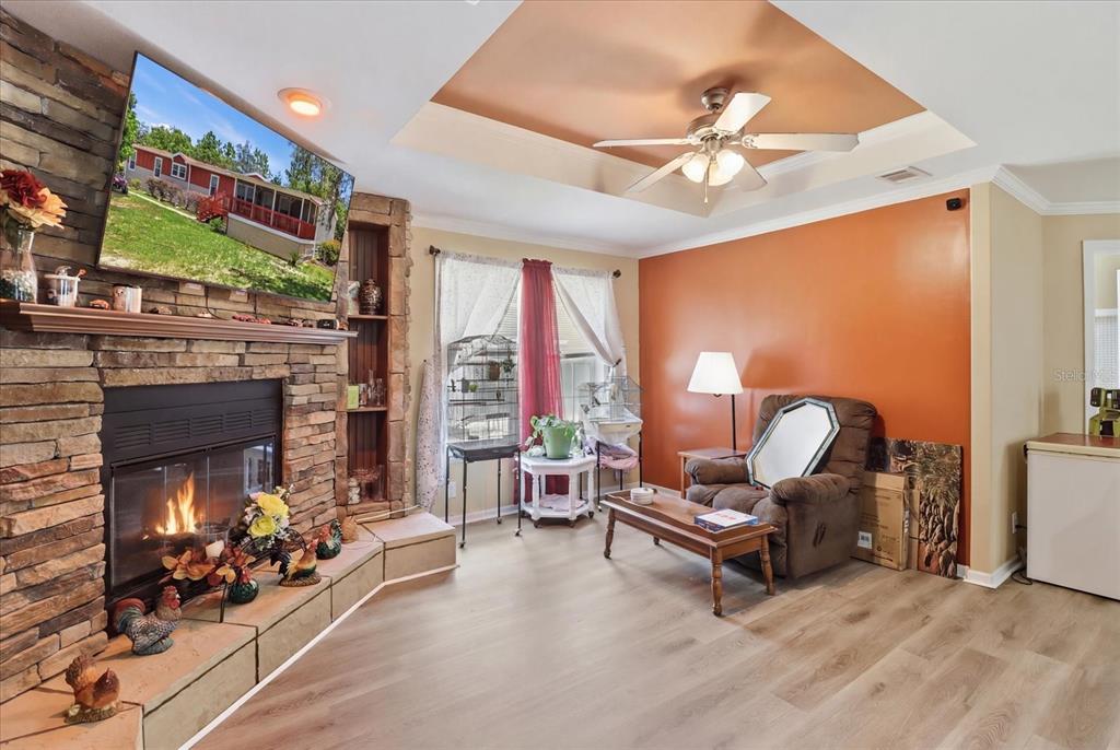 A living room features a stone fireplace, a television, a ceiling fan, and orange walls — 1391 S GETTYSBURG DRIVE, HOMOSASSA, FL