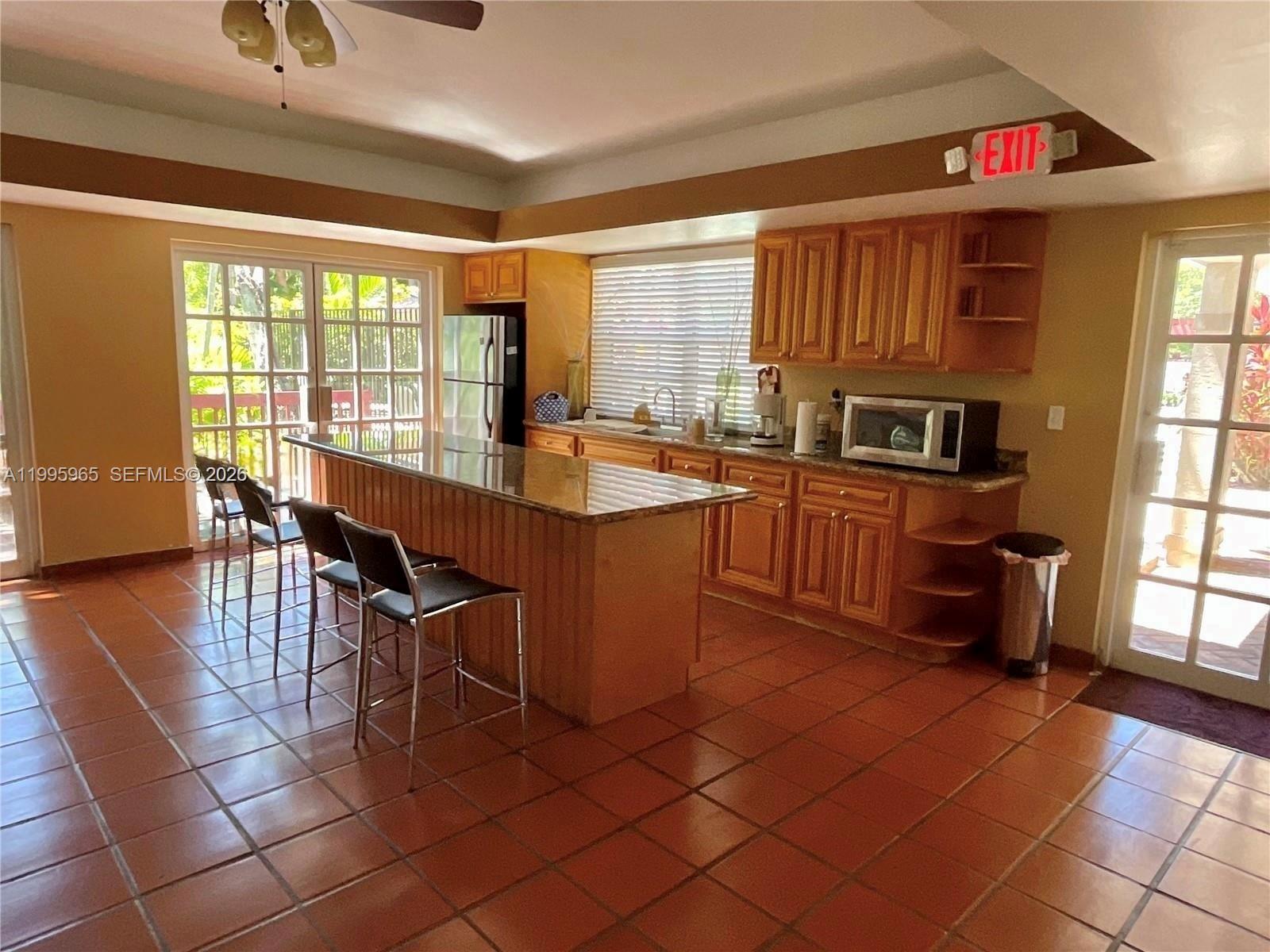 A kitchen features wood cabinets, granite countertops, a breakfast bar, and terracotta tile flooring — 9998 NOB HILL PL # 9998, Sunrise FL 33351, SUNRISE, FL