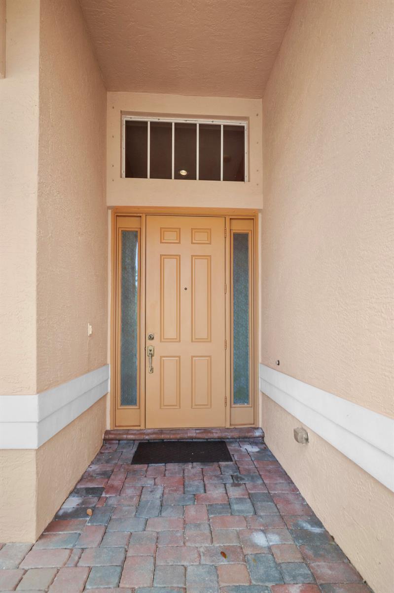 A beige front door with sidelights and a transom window sits on a paved porch — 1196 SE Fleming Way, Stuart FL 34997, STUART, FL