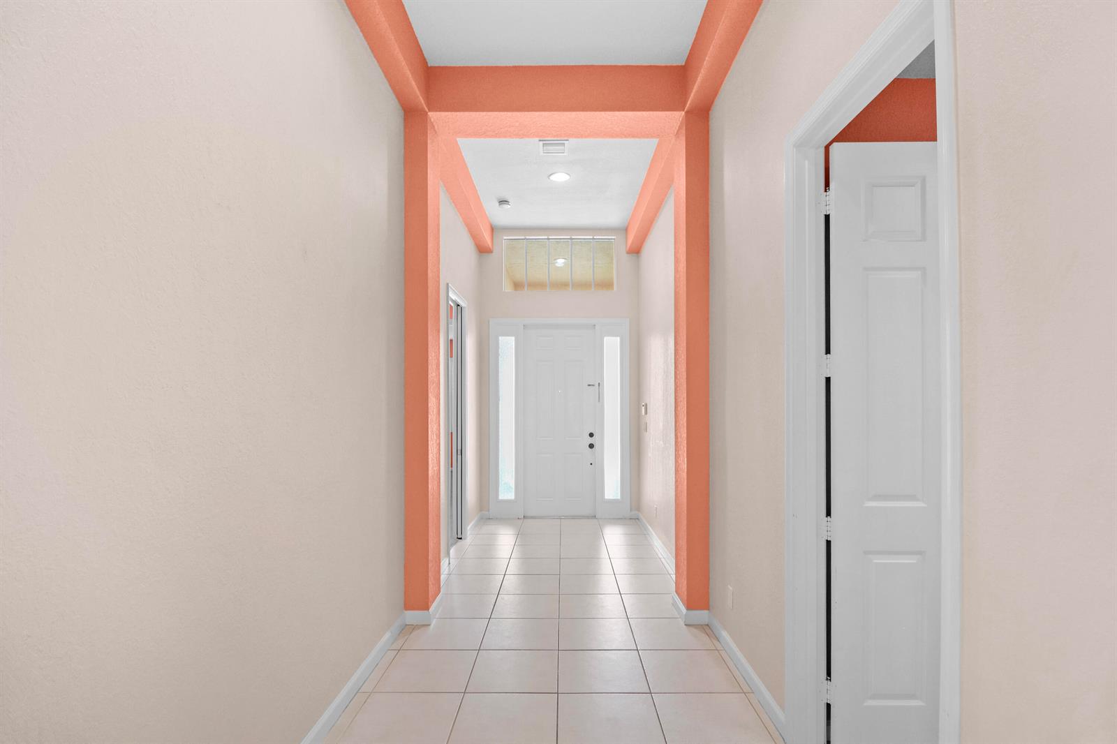 A hallway with light-colored tile flooring leads to a white front door with sidelights — 1196 SE Fleming Way, Stuart FL 34997, STUART, FL