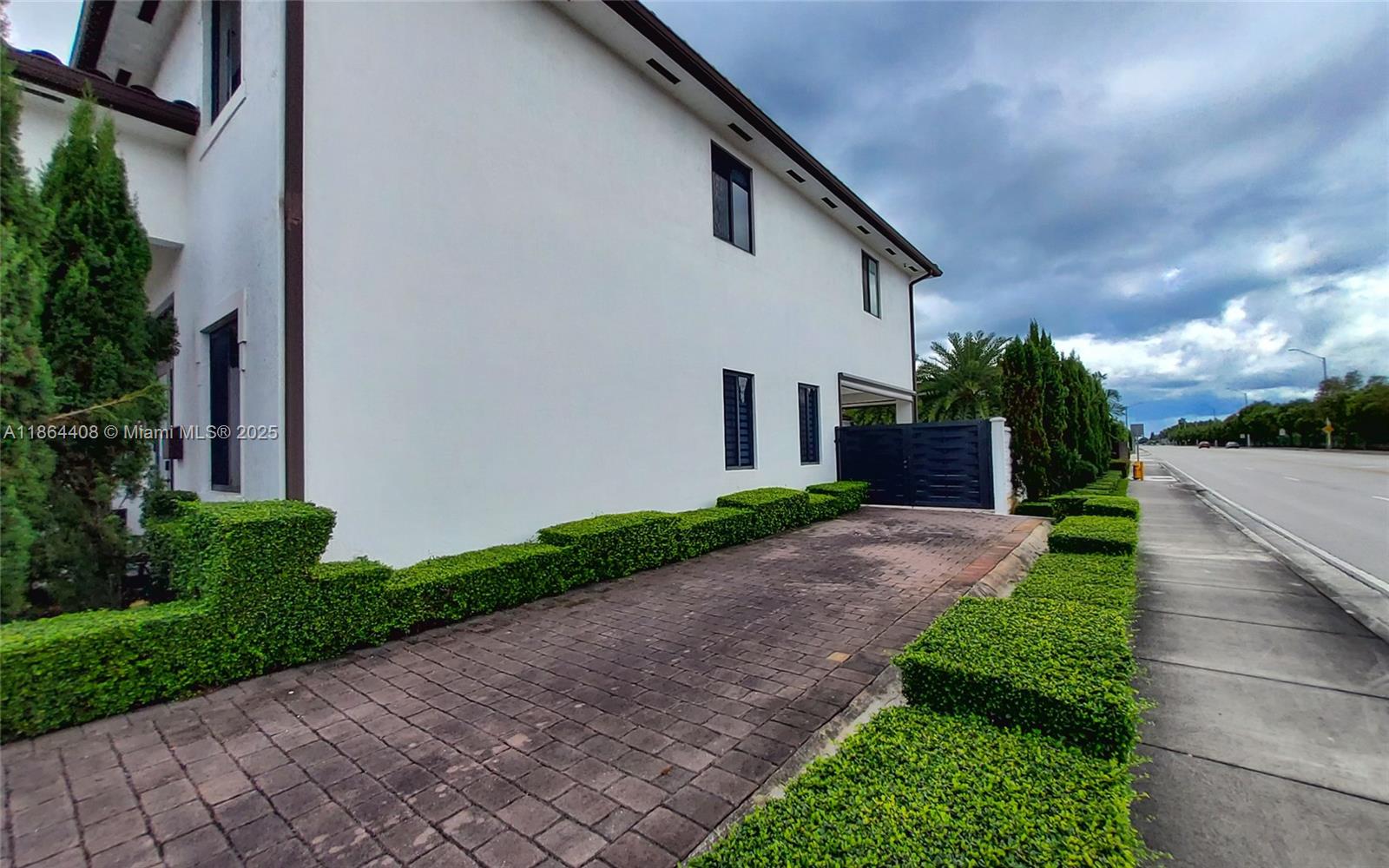A white two-story house features a paved driveway and manicured hedges along a roadside — 14680 SW 17th St, Miami FL 33175, MIAMI, FL