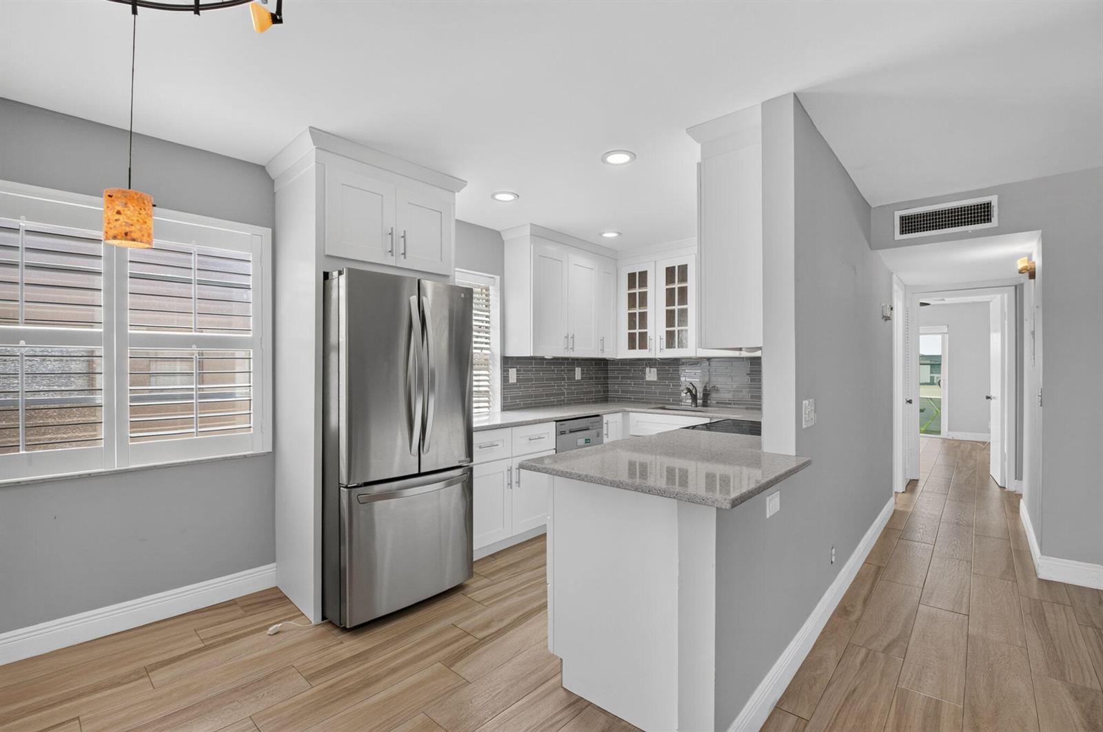 A kitchen features white cabinets, stainless steel appliances, gray tile backsplash, and light wood flooring — 374 Capri H, Delray Beach FL 33484, DELRAY BEACH, FL