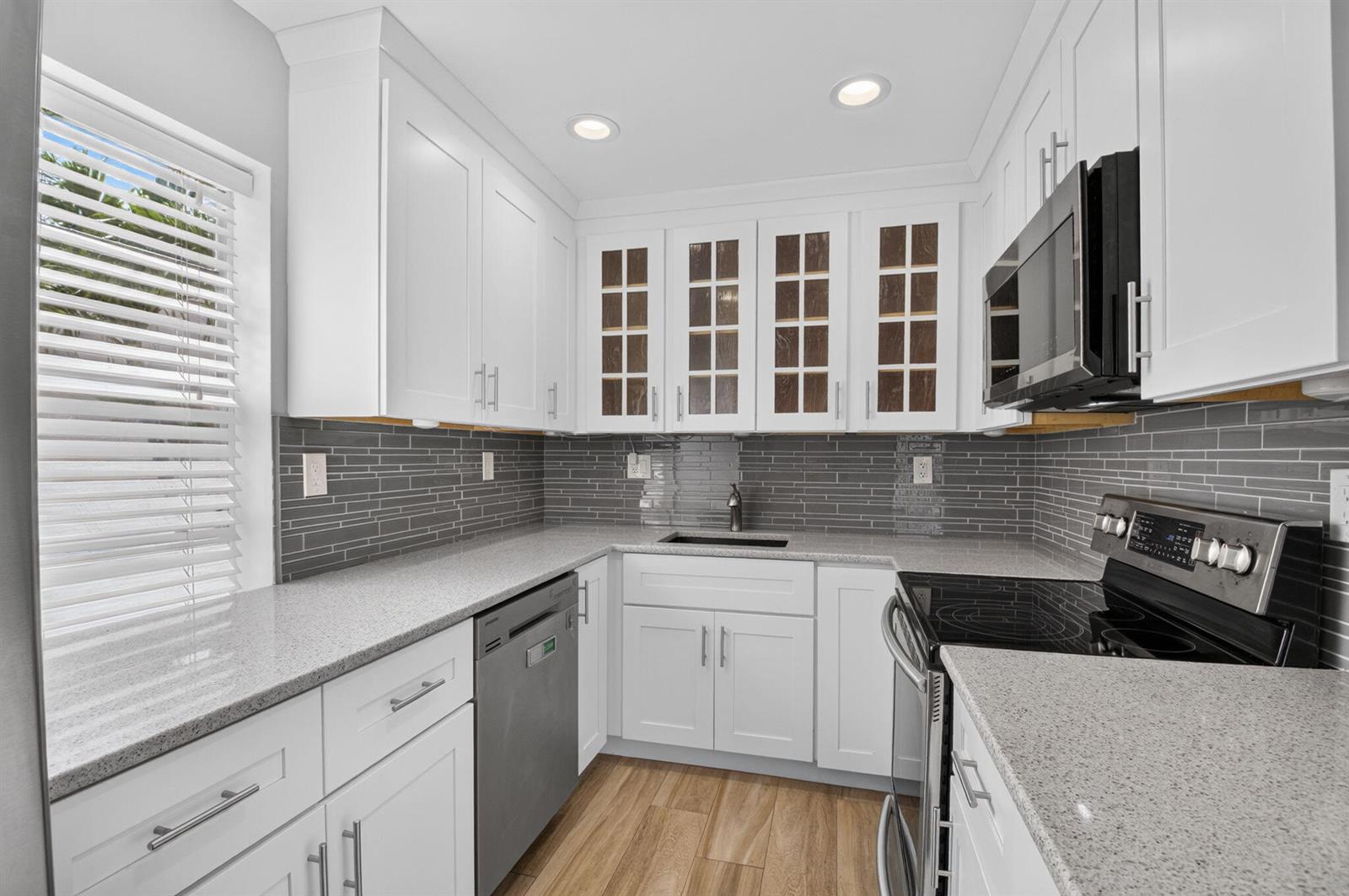 A kitchen features white cabinets, gray tile backsplash, granite countertops, and stainless steel appliances — 374 Capri H, Delray Beach FL 33484, DELRAY BEACH, FL