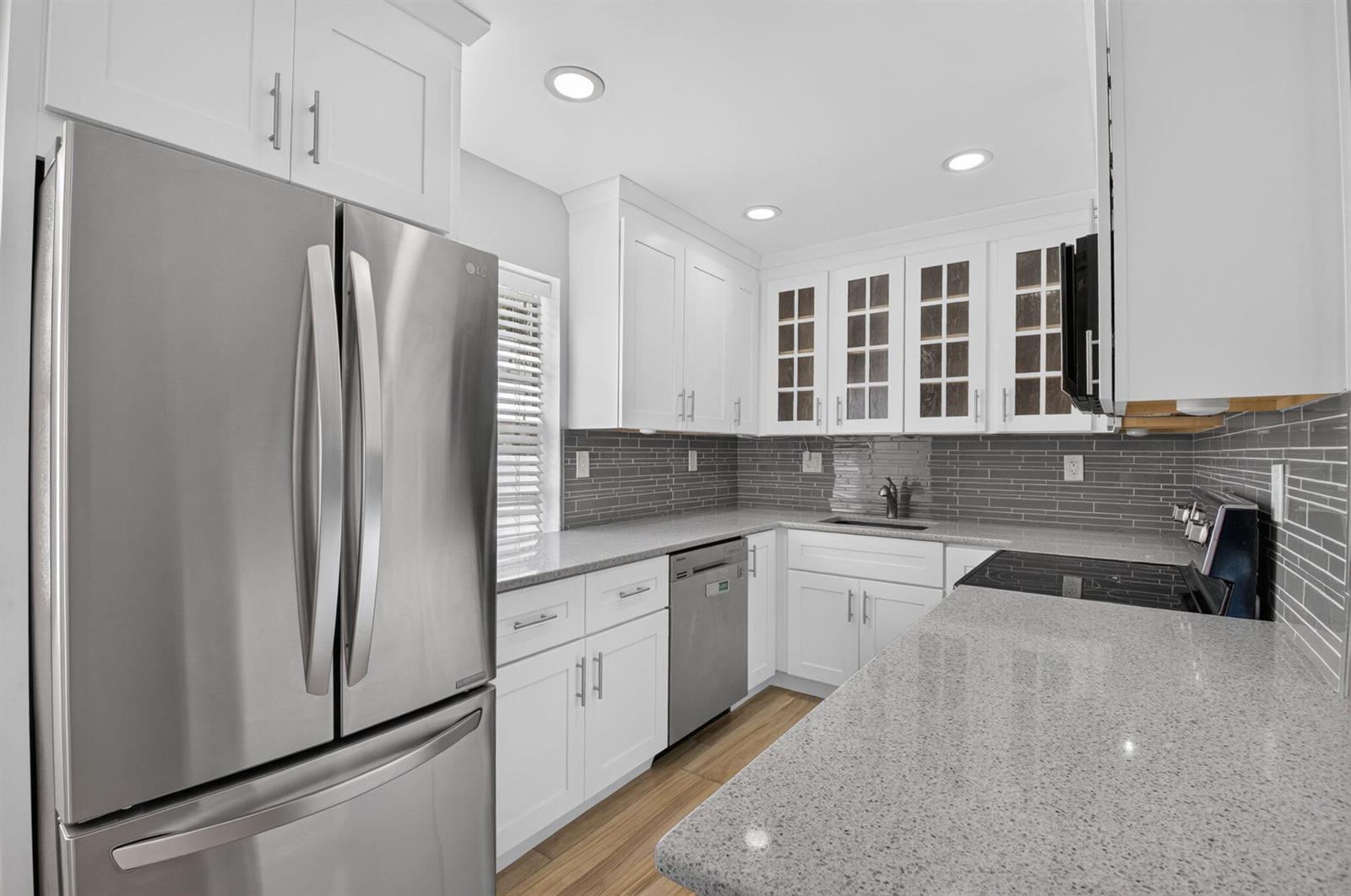 A kitchen features white cabinets, stainless steel appliances, gray tile backsplash, and speckled granite countertops — 374 Capri H, Delray Beach FL 33484, DELRAY BEACH, FL