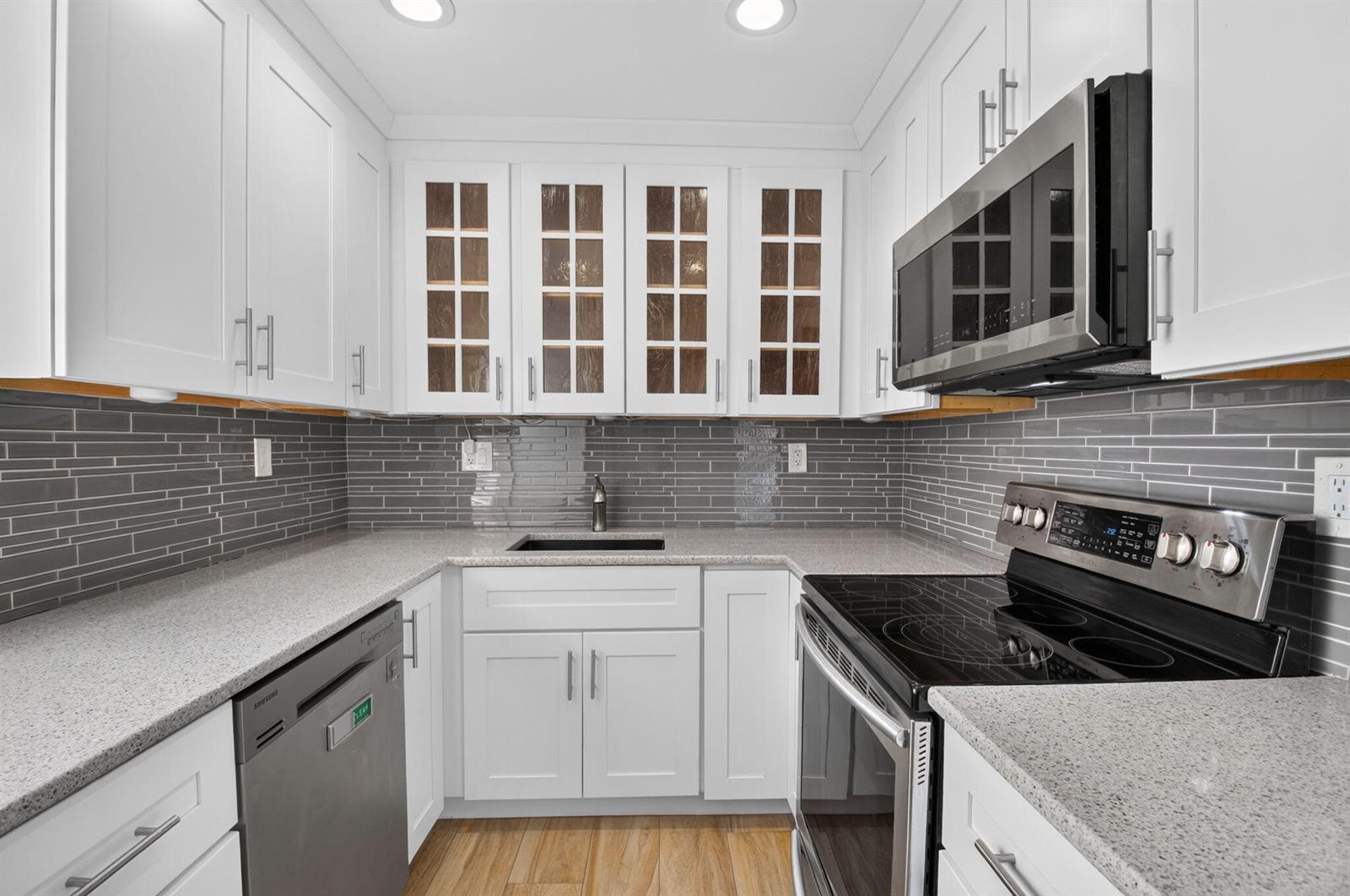 A kitchen features white cabinets, gray tile backsplash, stainless steel appliances, and speckled granite countertops — 374 Capri H, Delray Beach FL 33484, DELRAY BEACH, FL