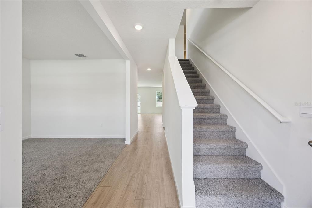 A carpeted staircase sits beside a hallway with wood-look flooring and a carpeted room — 1103 GULL DRIVE, APOPKA, FL