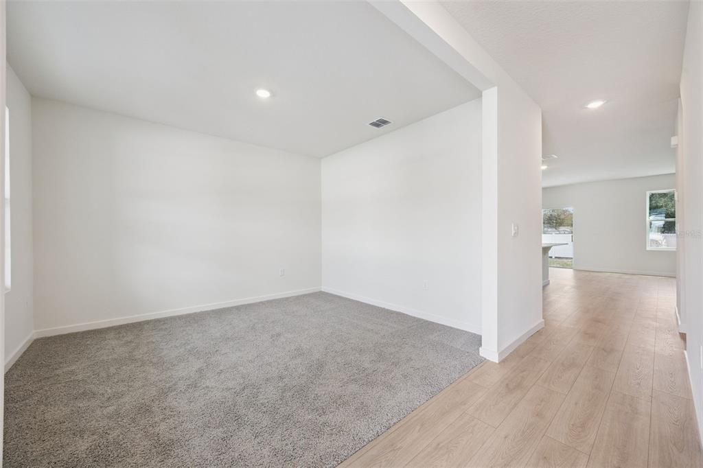 A carpeted room with white walls opens into a hallway with light wood-look flooring — 1103 GULL DRIVE, APOPKA, FL