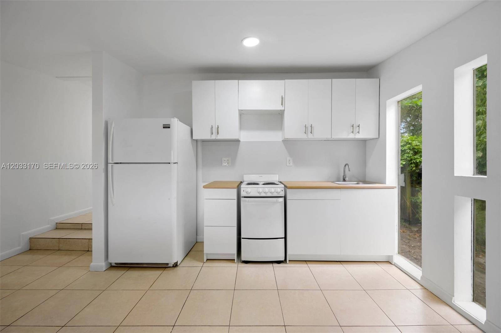 A kitchen features white cabinets, a refrigerator, a stove, and a sink on tiled floors — 348 NE 58th St # 1, Miami FL 33137, MIAMI, FL