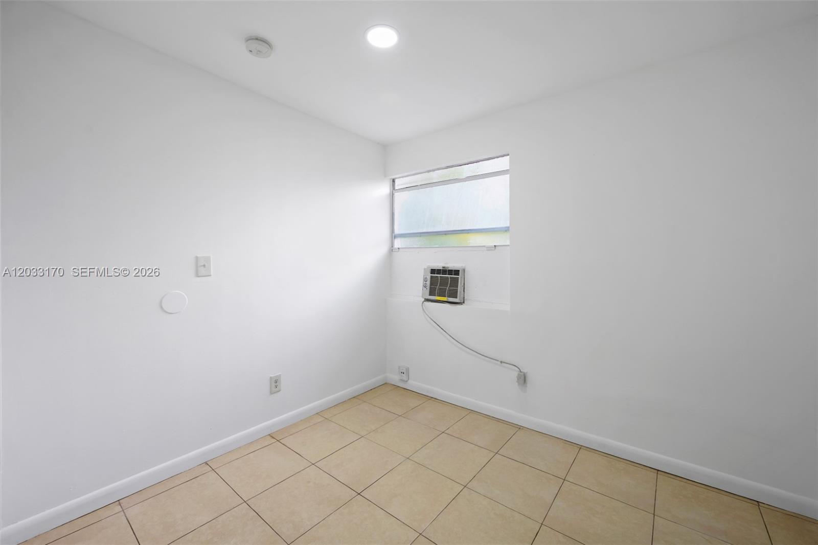 A small, empty room features white walls, beige tile flooring, and a window air conditioner — 348 NE 58th St # 1, Miami FL 33137, MIAMI, FL