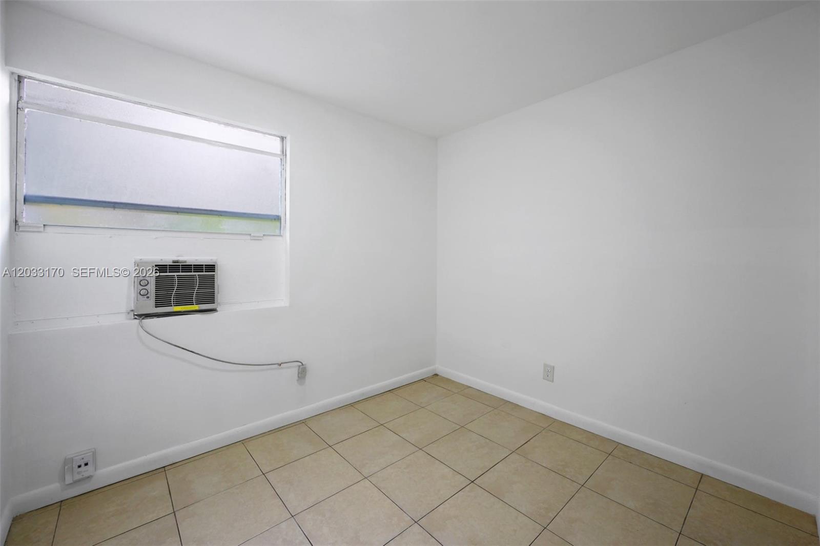 An empty room features white walls, beige tile flooring, and a window-mounted air conditioning unit — 348 NE 58th St # 1, Miami FL 33137, MIAMI, FL