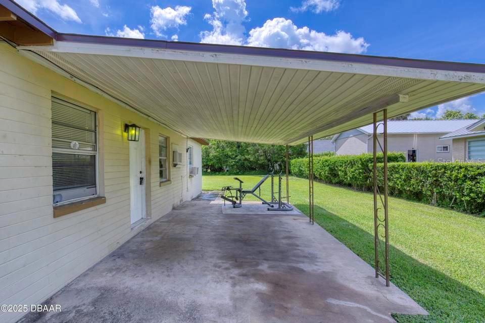 A covered concrete patio features a weight bench and overlooks a grassy backyard — 815 8TH STREET, DAYTONA BEACH, FL