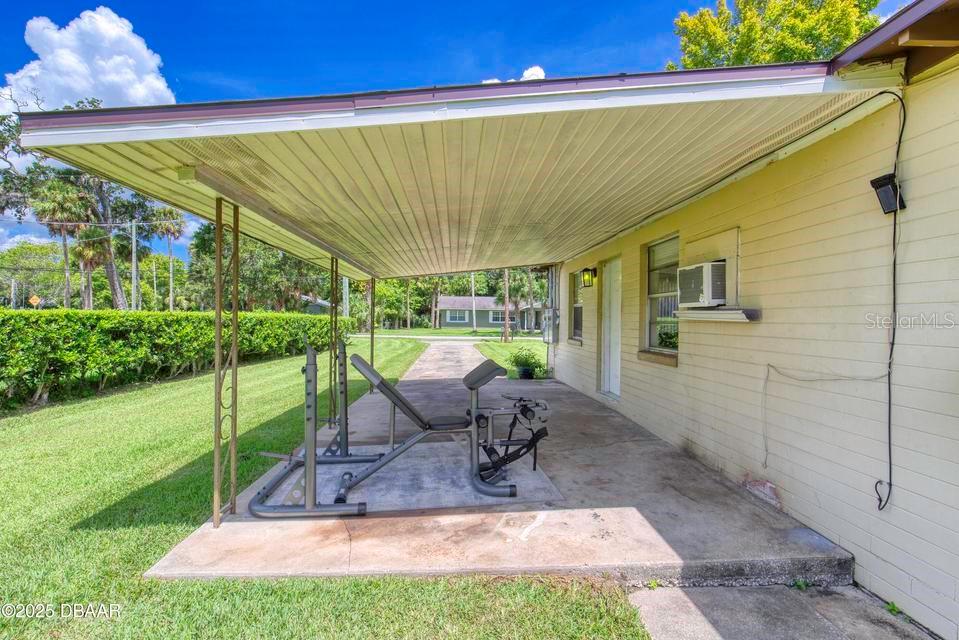 A concrete carport attached to a yellow house features a weight bench set — 815 8TH STREET, DAYTONA BEACH, FL