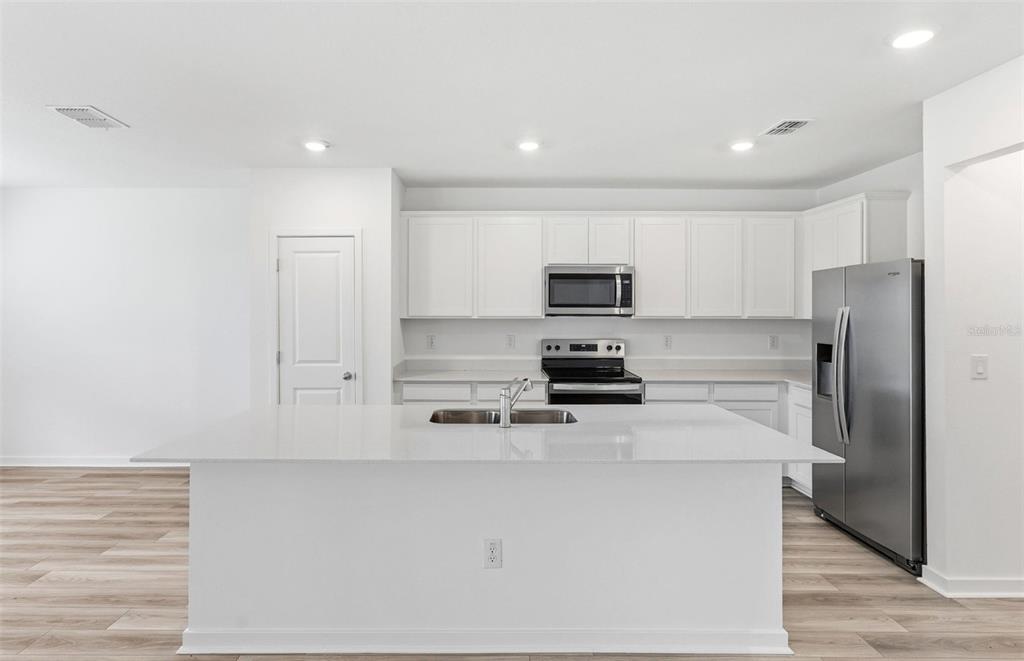 A modern kitchen features a large white island, stainless steel appliances, and white cabinetry — 10410 HIDDEN BANKS GLEN, PARRISH, FL
