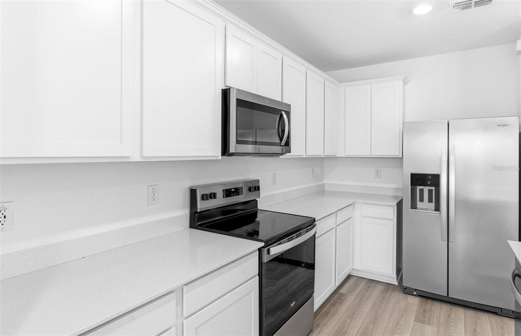A modern kitchen features white cabinets, stainless steel appliances, and light-colored countertops — 10410 HIDDEN BANKS GLEN, PARRISH, FL