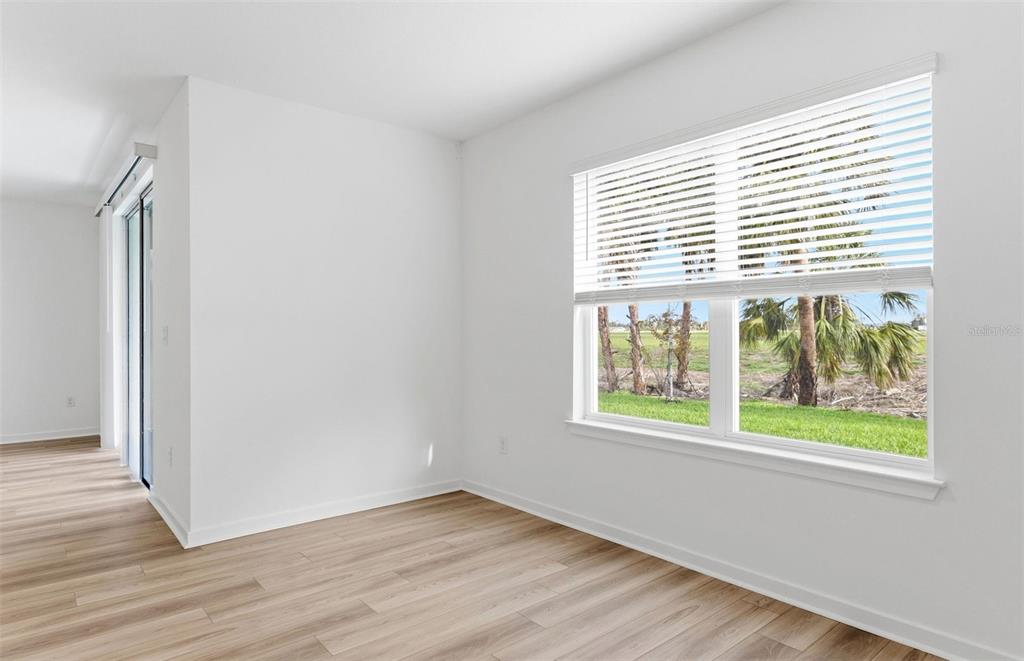 An empty room with light wood-look flooring, white walls, and a window overlooking palm trees — 10410 HIDDEN BANKS GLEN, PARRISH, FL
