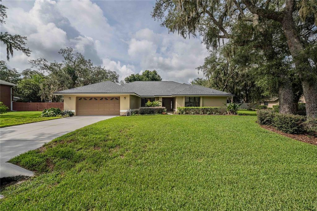 A single-story house with a tan exterior, a two-car garage, and a large front lawn — 1749 LADY BOWERS TRAIL, LAKELAND, FL