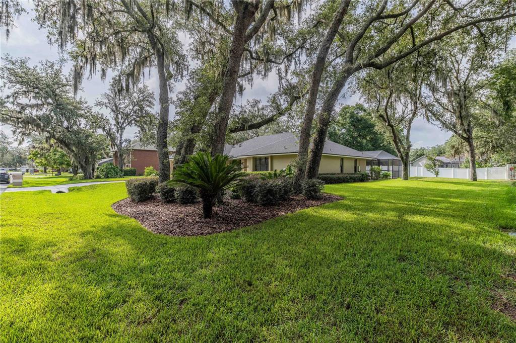 A single-story house sits behind a large lawn with mature trees and a landscaped bed — 1749 LADY BOWERS TRAIL, LAKELAND, FL