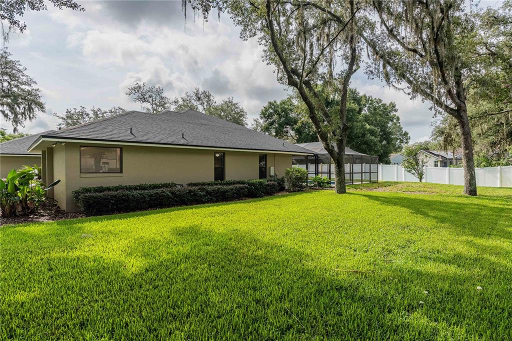 A view of a house exterior with a large lawn, trees, and a pool enclosure — 1749 LADY BOWERS TRAIL, LAKELAND, FL