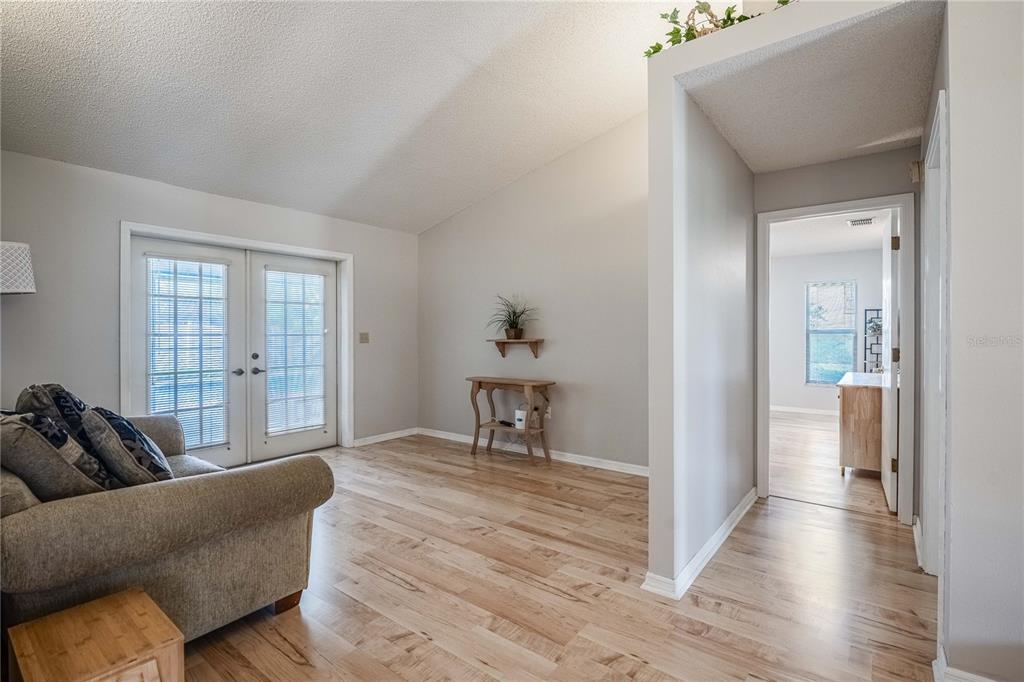 A living room with light wood flooring, vaulted ceilings, and French doors leading outside — 1749 LADY BOWERS TRAIL, LAKELAND, FL