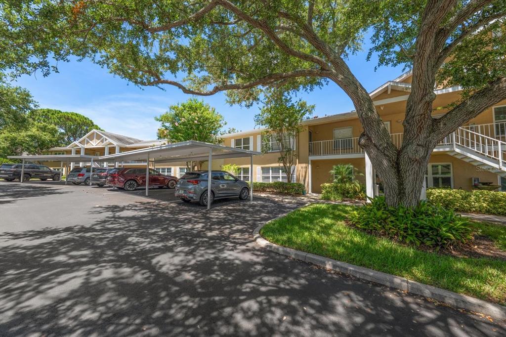 An exterior view of a two-story apartment building with covered parking and large shade trees — 2152 GULF VIEW BOULEVARD UNIT 2152, DUNEDIN, FL