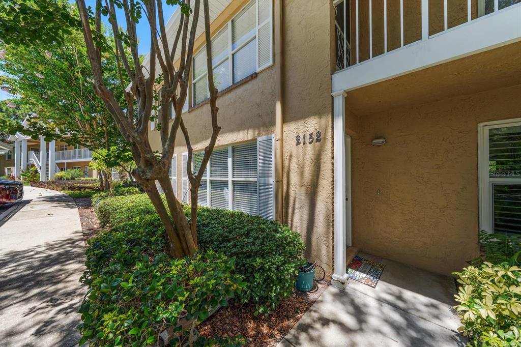 A tan two-story building exterior features a ground-level entrance, white shutters, and landscaping — 2152 GULF VIEW BOULEVARD UNIT 2152, DUNEDIN, FL