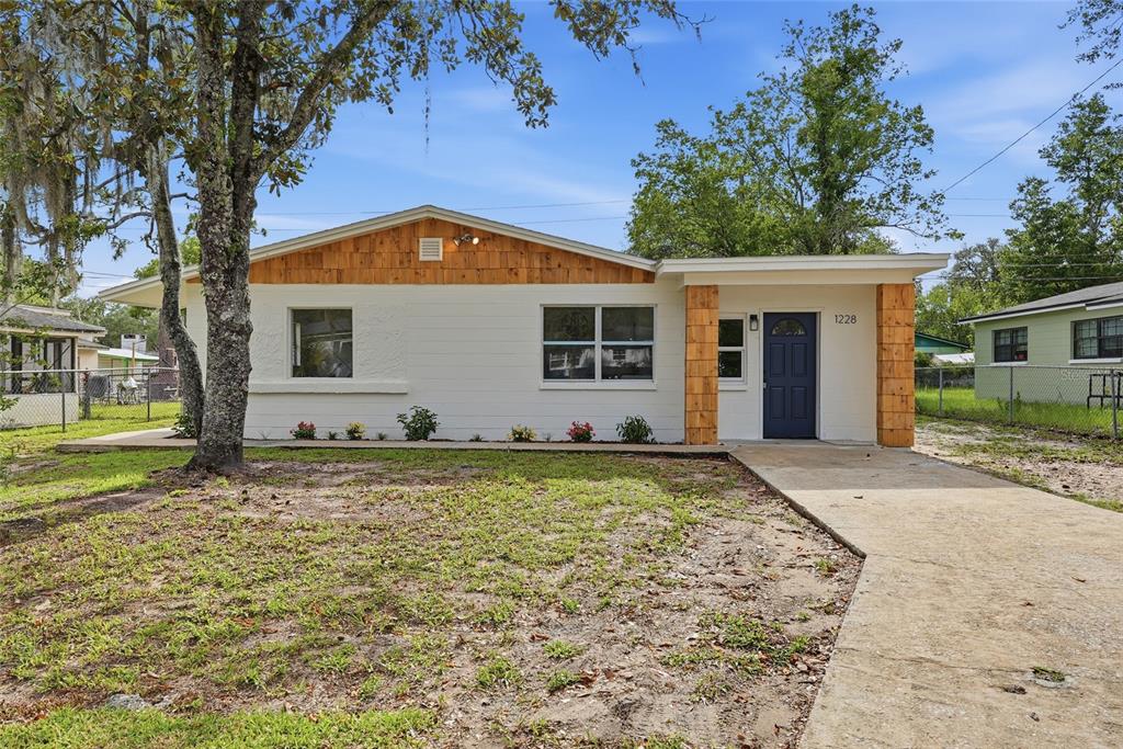 A single-story house with white painted brick, wood accents, and a dark blue front door — 1228 SE 19TH STREET, GAINESVILLE, FL