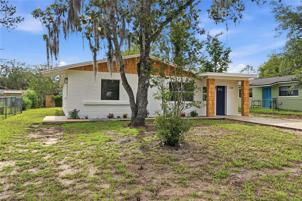 A single-story white house with wood-paneled accents and a blue front door — 1228 SE 19TH STREET, GAINESVILLE, FL