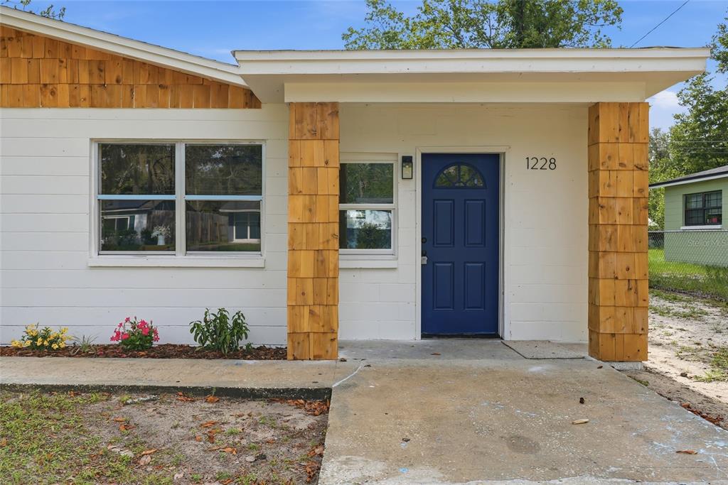 A white house exterior features a blue front door, wood-shingled columns, and a concrete walkway — 1228 SE 19TH STREET, GAINESVILLE, FL
