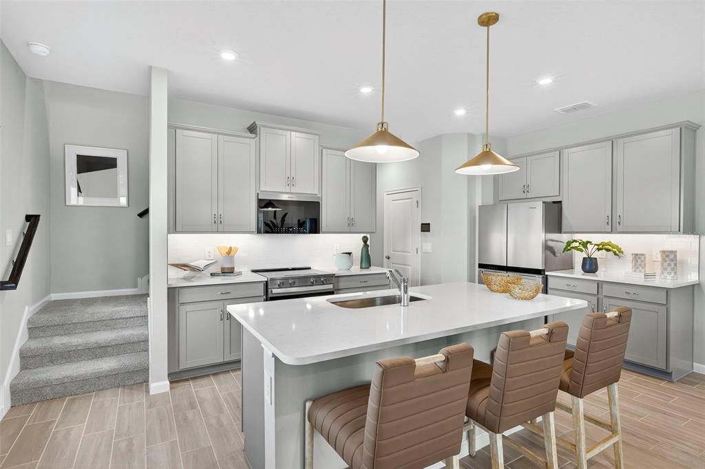 A modern kitchen features gray cabinets, white countertops, a central island, and three brown stools — 8851 GINKO RUN, PARRISH, FL