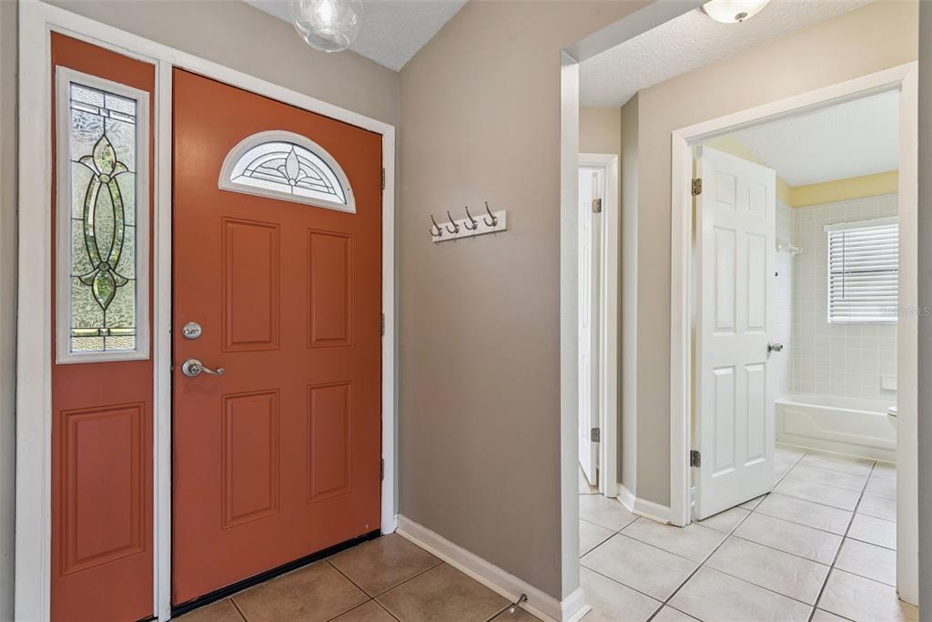 An entryway with a terracotta-colored front door, tile flooring, and a view into a bathroom — 1574 MARGARETE CRESCENT DRIVE, APOPKA, FL