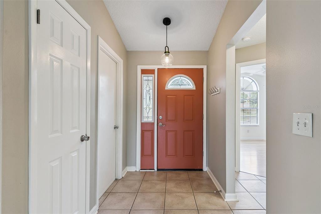 An entryway features a terracotta-colored front door, tiled flooring, and a hanging pendant light — 1574 MARGARETE CRESCENT DRIVE, APOPKA, FL