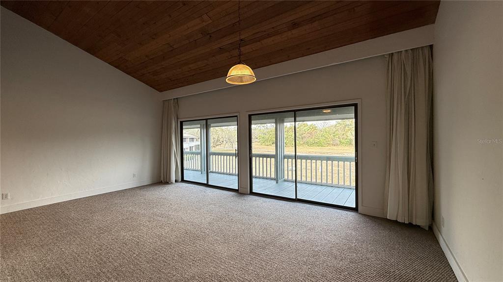 A room with a vaulted wood-plank ceiling, beige carpeting, and sliding glass doors to a deck — 176 PALM VIEW COURT UNIT 3475/6, HAINES CITY, FL