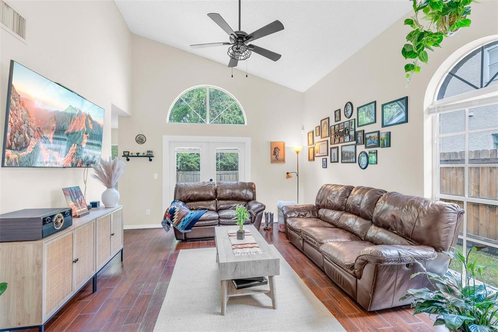 A living room features vaulted ceilings, brown leather sofas, a television, and a gallery wall — 10561 SATINWOOD CIRCLE, ORLANDO, FL