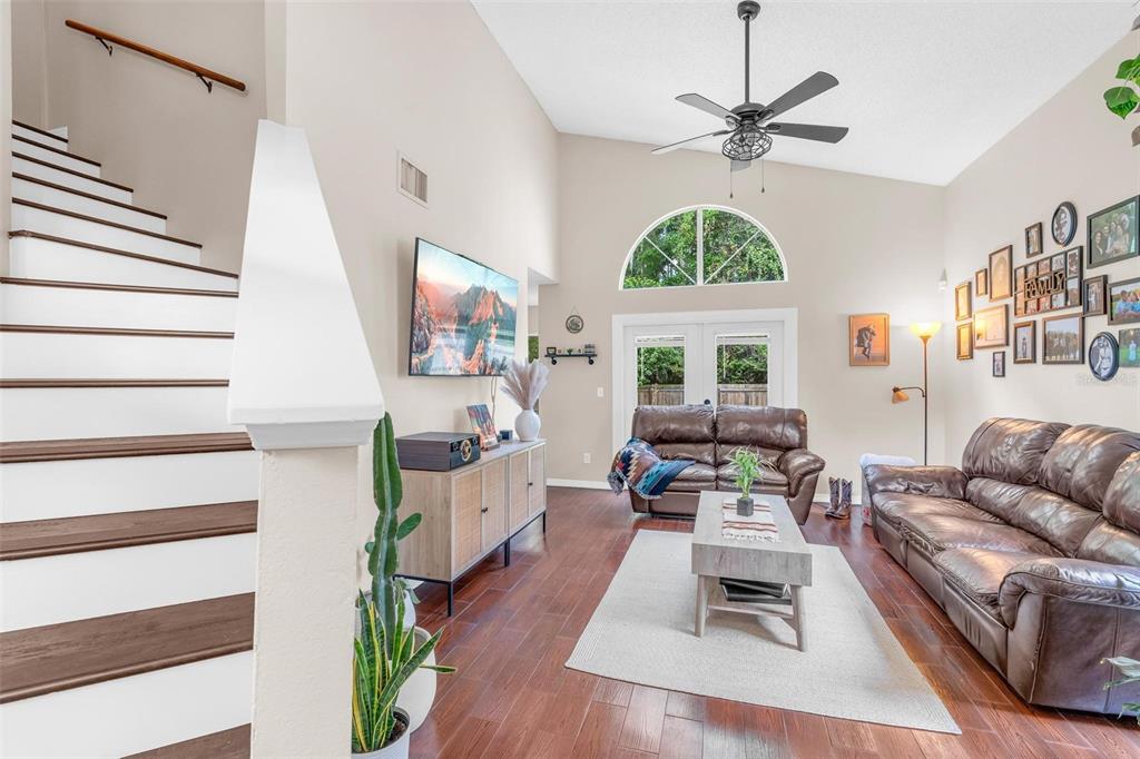 A living room features vaulted ceilings, a staircase, brown leather sofas, and hardwood flooring — 10561 SATINWOOD CIRCLE, ORLANDO, FL