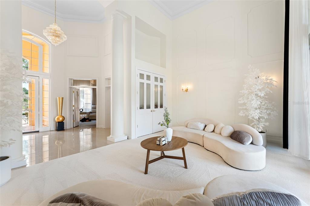 A bright, high-ceilinged living room features a curved cream sofa, round coffee table, and columns — 1274 PRINCE COURT, LAKE MARY, FL