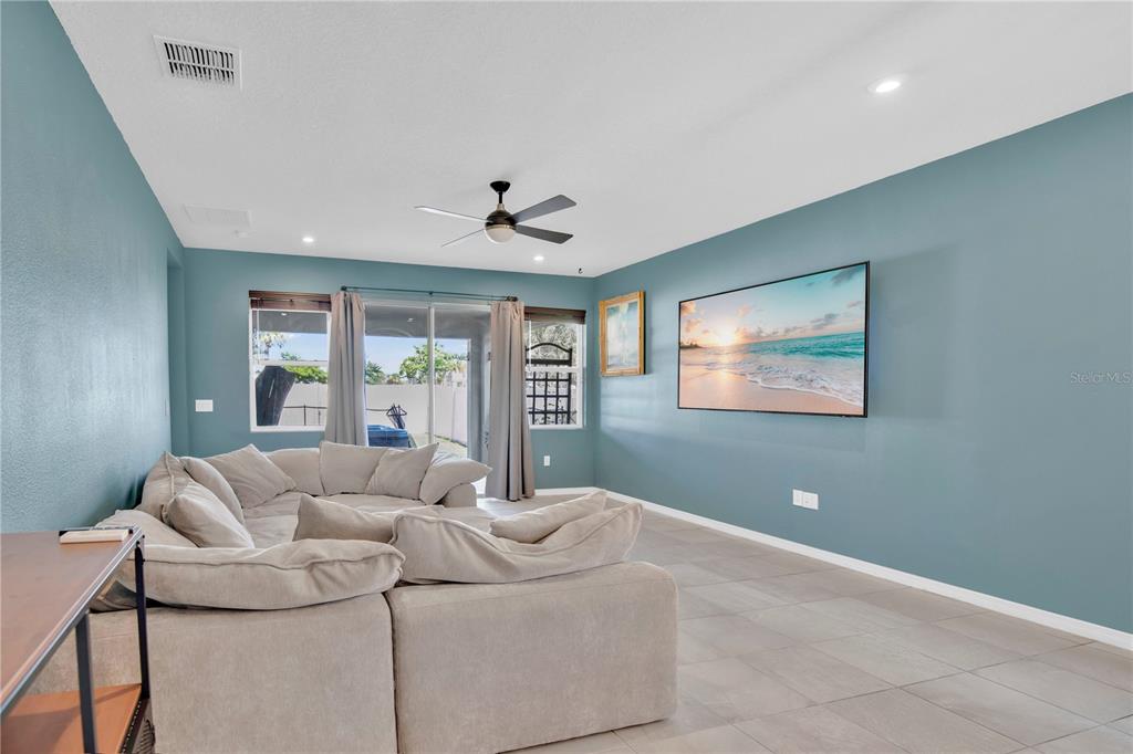 A living room features blue walls, a large sectional sofa, tile flooring, and a wall-mounted television — 2203 GARDEN BELLE DRIVE, CLERMONT, FL