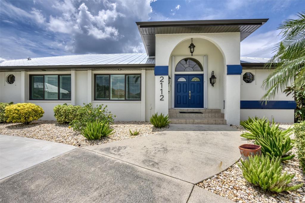 The exterior of a single-story house features a blue double door under an arched entryway — 2112 DEBORAH DRIVE, PUNTA GORDA, FL