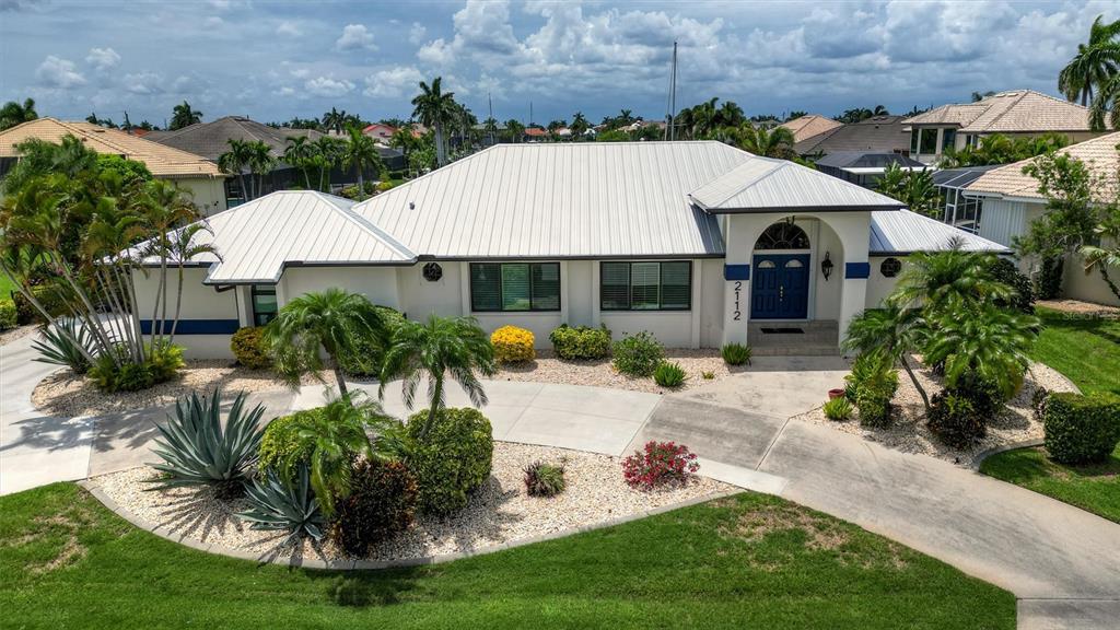 A single-story house with a white metal roof, blue double doors, and a landscaped driveway — 2112 DEBORAH DRIVE, PUNTA GORDA, FL