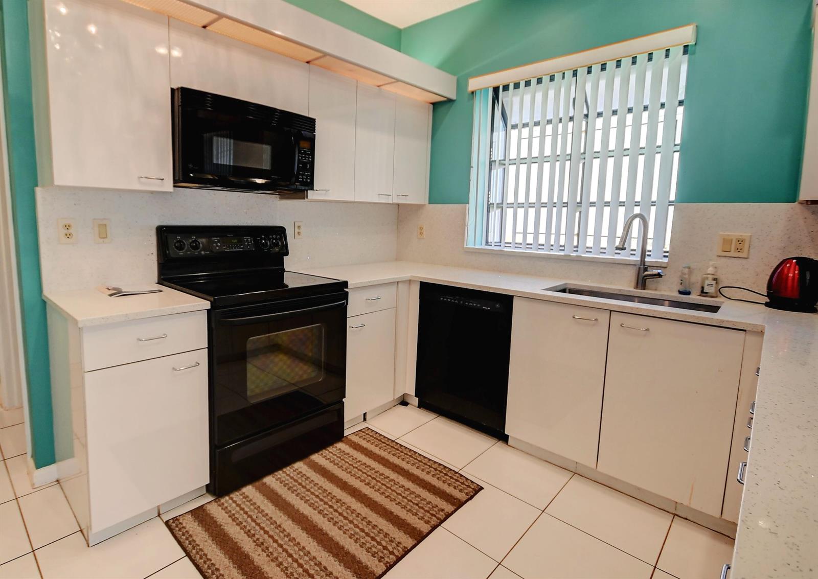 A kitchen with white cabinets, black appliances, teal walls, and light-colored countertops — 19356 Cherry Hills Terrace, Boca Raton FL 33498, BOCA RATON, FL