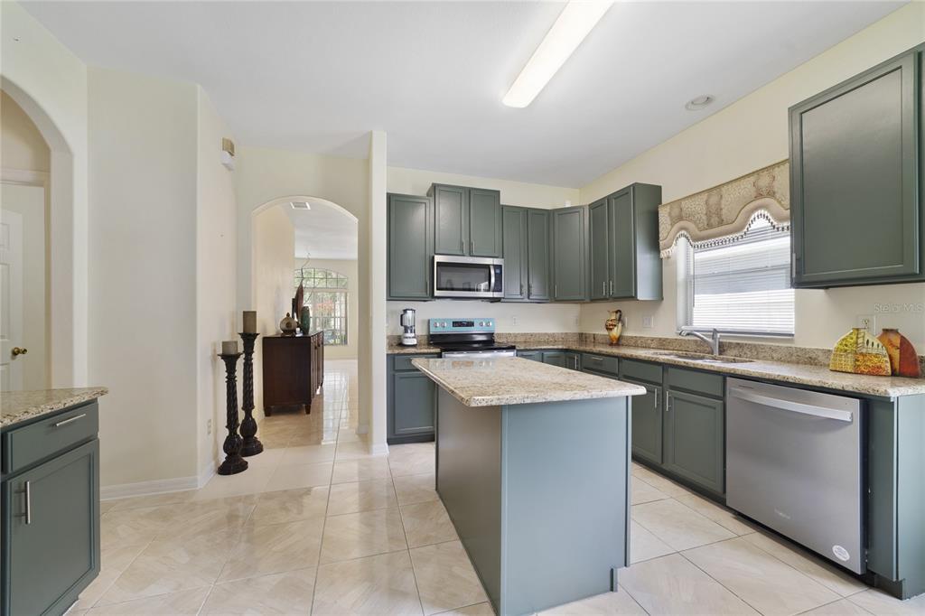 A kitchen features green cabinets, granite countertops, a central island, and stainless steel appliances — 8376 PORT LANCASHIRE DRIVE, ORLANDO, FL