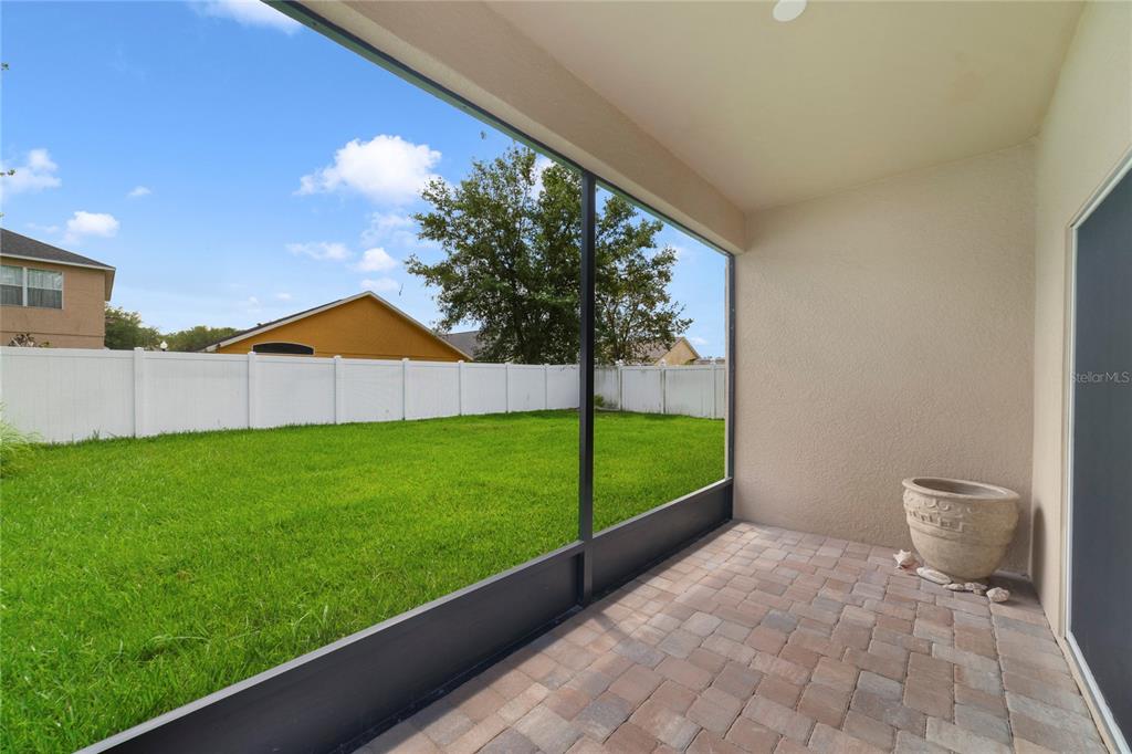 A screened-in patio with paver flooring overlooks a grassy backyard enclosed by a white fence — 8376 PORT LANCASHIRE DRIVE, ORLANDO, FL