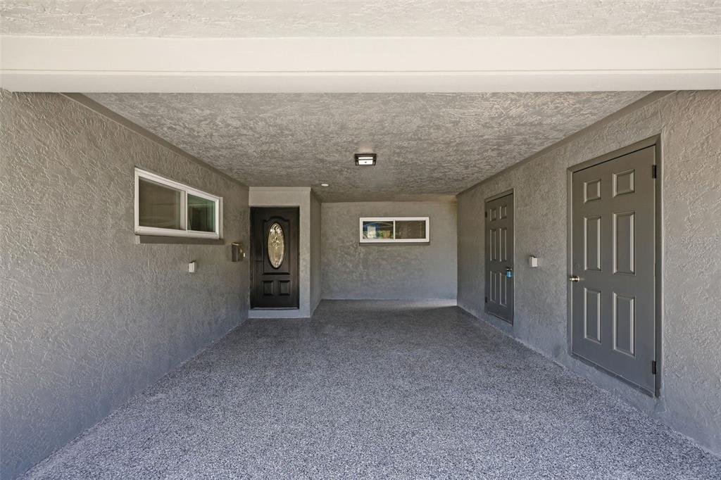 A covered carport features gray stucco walls, a textured ceiling, and three dark doors — 4435 HUNTINGTON STREET NE, ST PETERSBURG, FL