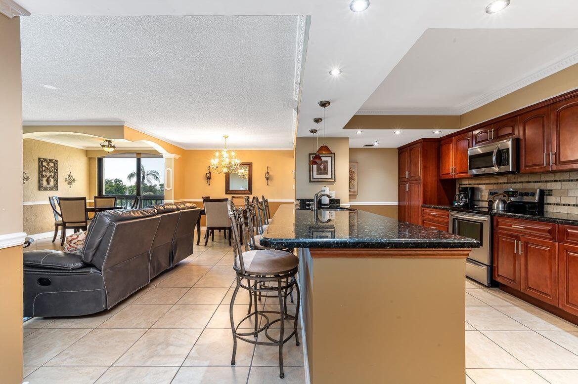 An open-concept kitchen with dark wood cabinets and a granite island overlooks a living area — 1915 Lavers Circle, Delray Beach FL 33444, DELRAY BEACH, FL