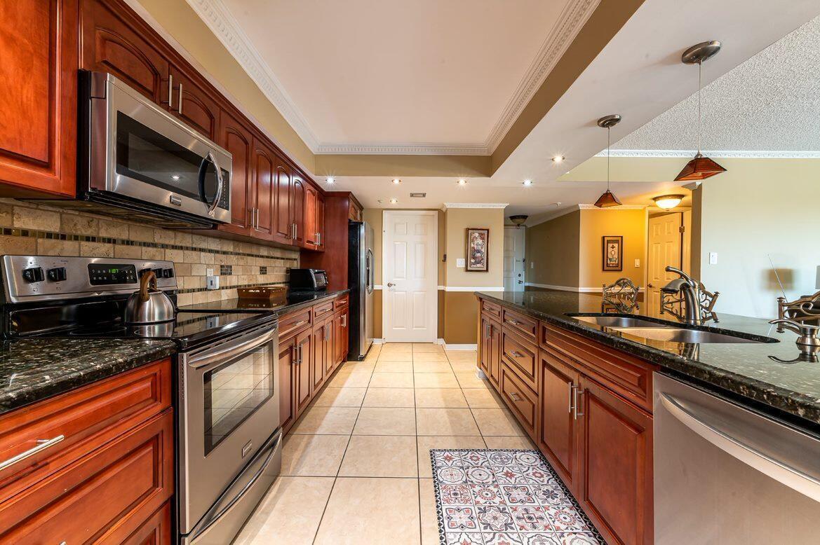 A kitchen features dark wood cabinets, granite countertops, stainless steel appliances, and tiled flooring — 1915 Lavers Circle, Delray Beach FL 33444, DELRAY BEACH, FL