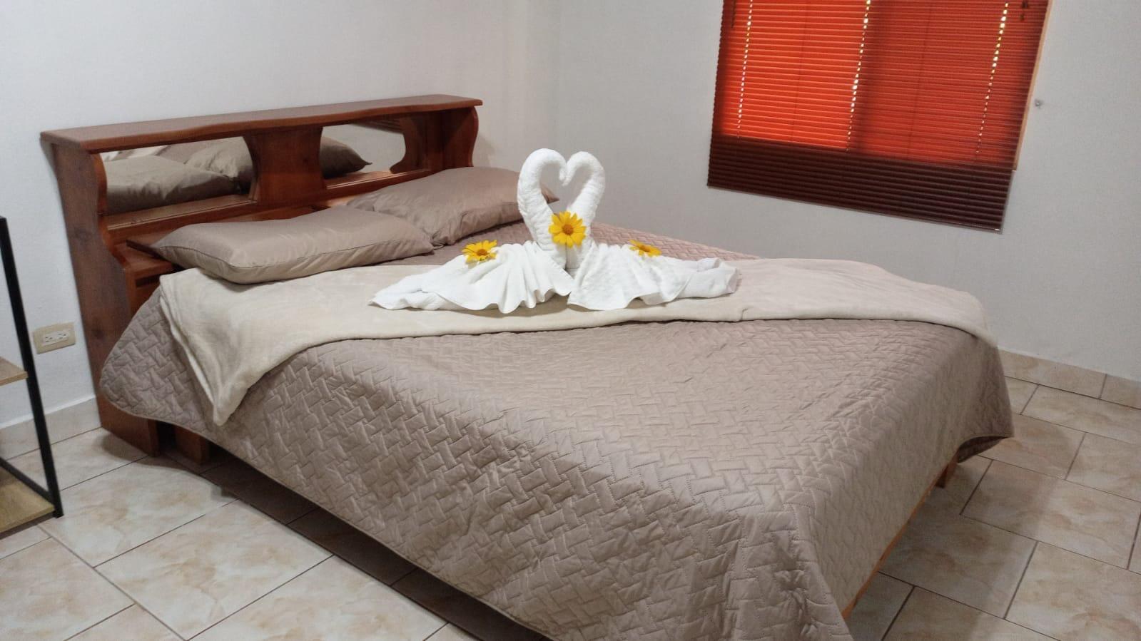 A bedroom features a wooden headboard, a bed with towel swans, and orange window blinds — 0000 Hope Garden, 00000, FL