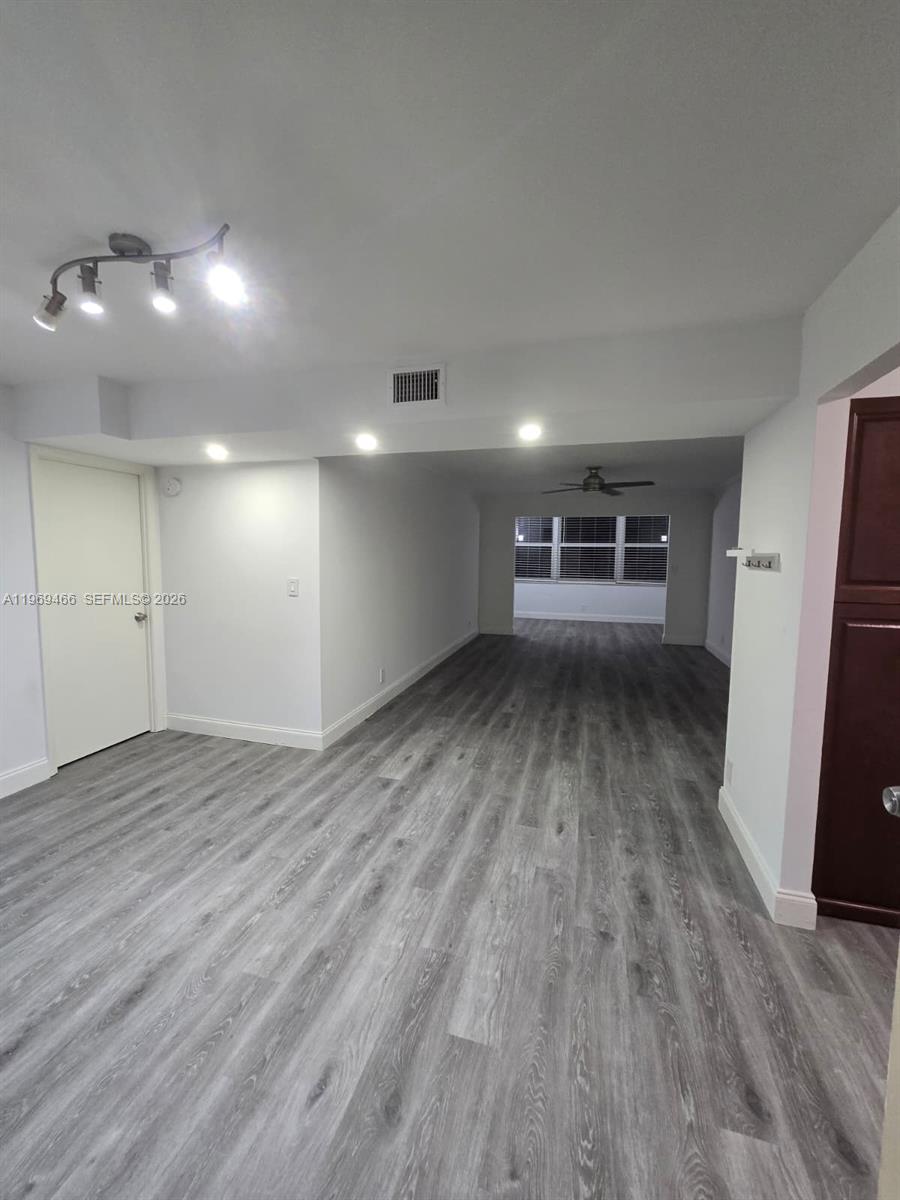 An empty room features gray wood-look flooring, white walls, and a modern track lighting fixture — 6500 Cypress Rd # 301, Plantation FL 33317, PLANTATION, FL