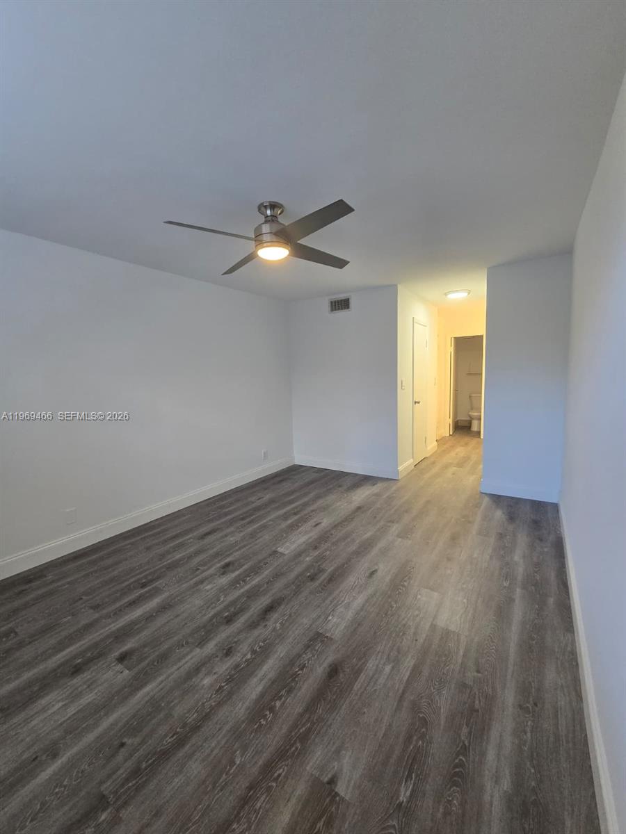 An empty room features gray wood-look flooring, a ceiling fan, and a hallway leading to a bathroom — 6500 Cypress Rd # 301, Plantation FL 33317, PLANTATION, FL