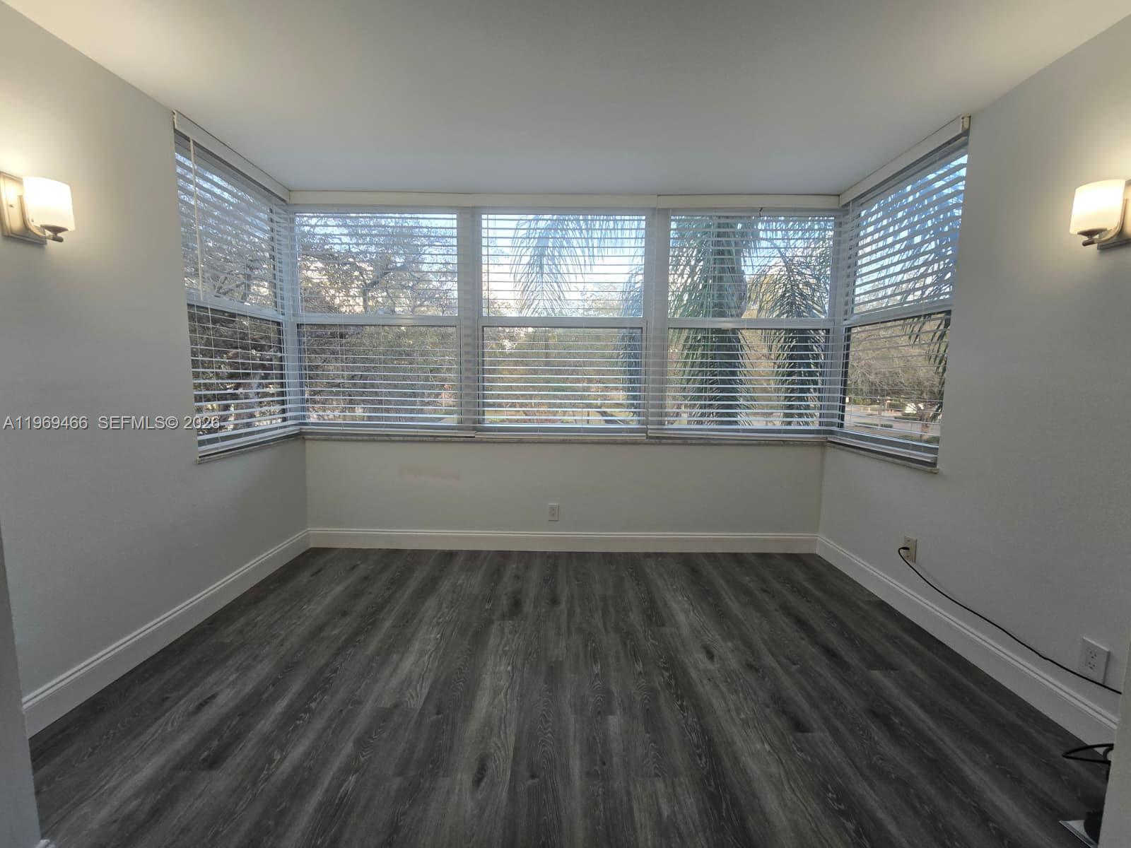An empty room features gray wood-look flooring, light-colored walls, and a large bay window — 6500 Cypress Rd # 301, Plantation FL 33317, PLANTATION, FL